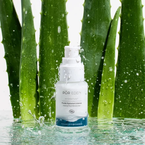 Fluide Hydratant Intense PUR EDEN devant des feuilles d’aloe vera avec éclaboussures d’eau pour illustrer son pouvoir hydratant